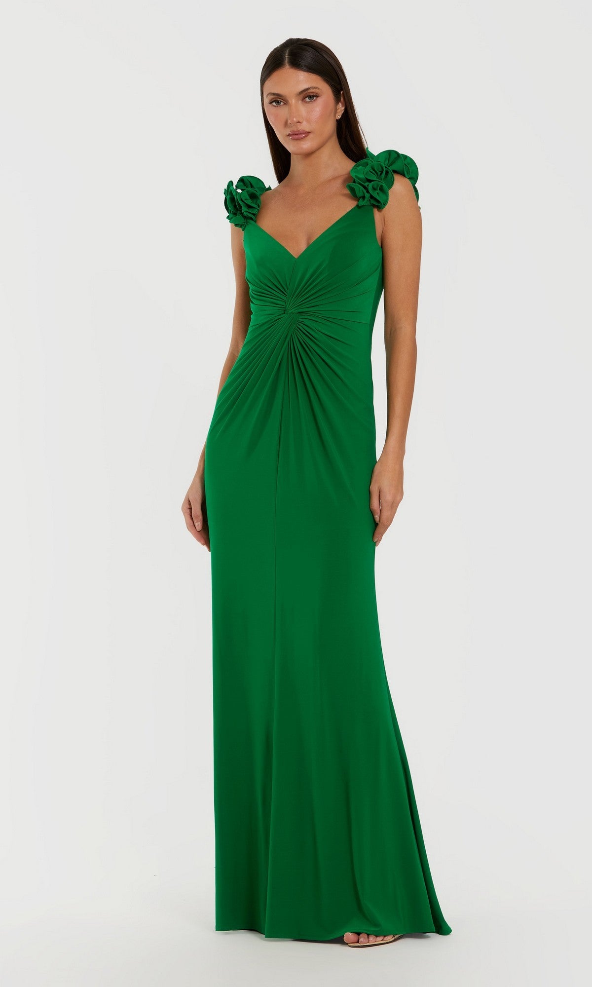 A woman wearing the Mac Duggal 44094 Long Formal Dress in Spring Green, featuring a floor-length, fitted silhouette with gathered detailing at the waist and eye-catching 3D shoulder straps embellished with floral accents, stands against a plain white background.